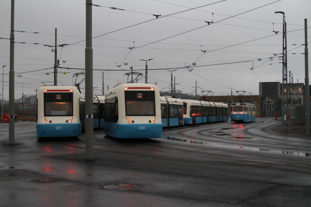 Tre spårvagnar står uppställda i regnet utanför den nybyggda spårvagnsdepån.